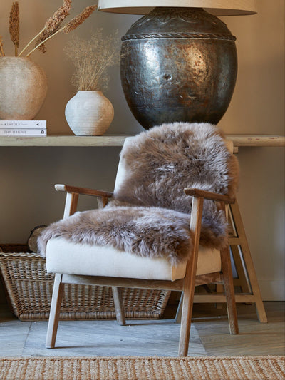 Chair with taupe sheepskin rug in a room with a lamp and decorative items on a table.