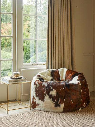 Cowhide beanbag in a room with large windows and beige curtains.