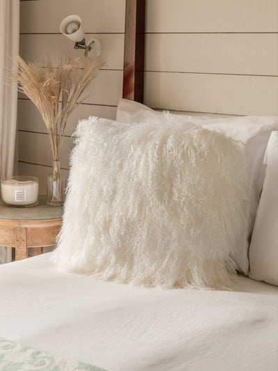 Fluffy Tibetan sheepskin cushion on a bed with a wooden headboard and decorative elements.