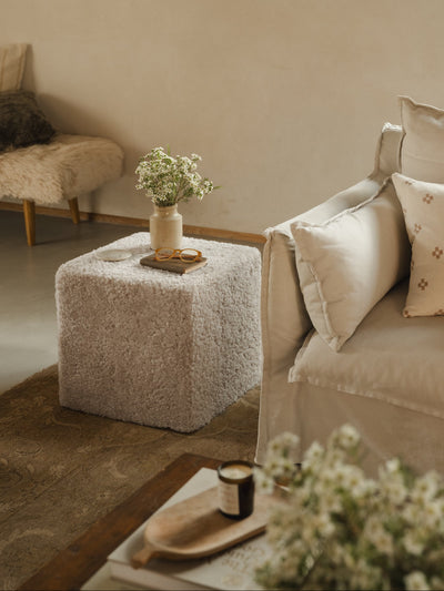 Cosy living room with a beige sofa, sheepskin pouffe, and decorative items.