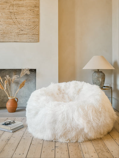 White Tibetan sheepskin beanbag chair in a room with a fireplace and lamp.