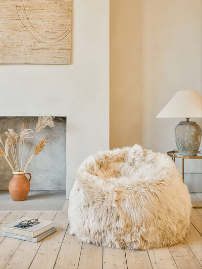 Fluffy white wool beanbag in a room with a fireplace, lamp, and decorative items.
