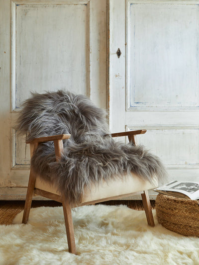 Chair with a Icelandic sheepskin rug in a room with wooden doors and a wicker basket.
